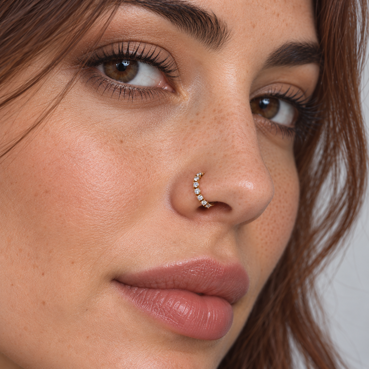 Model wearing a petite gold hoop nose ring with seven clear crystals