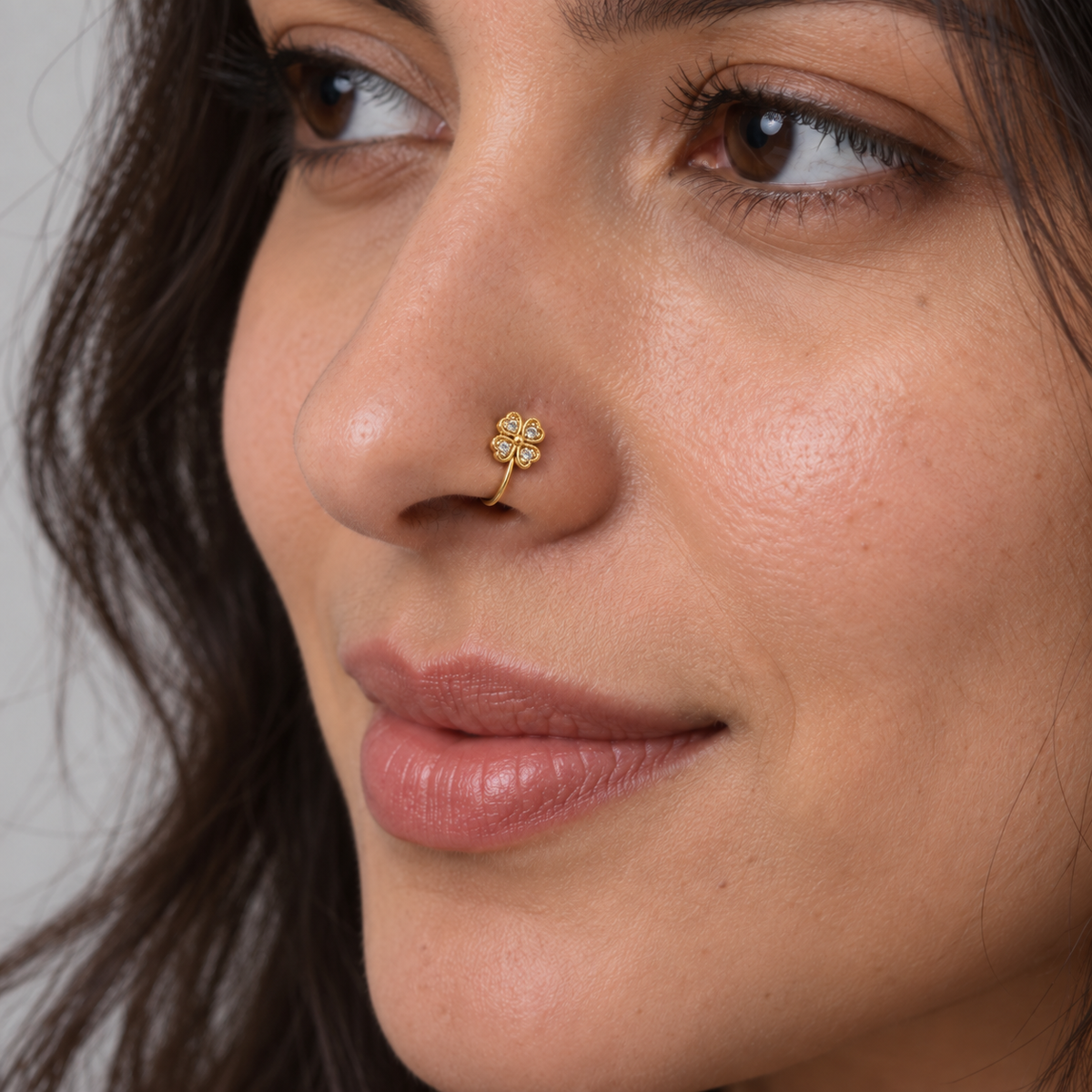 Woman wearing a petite gold four-leaf crystal clover clip-on nose ring