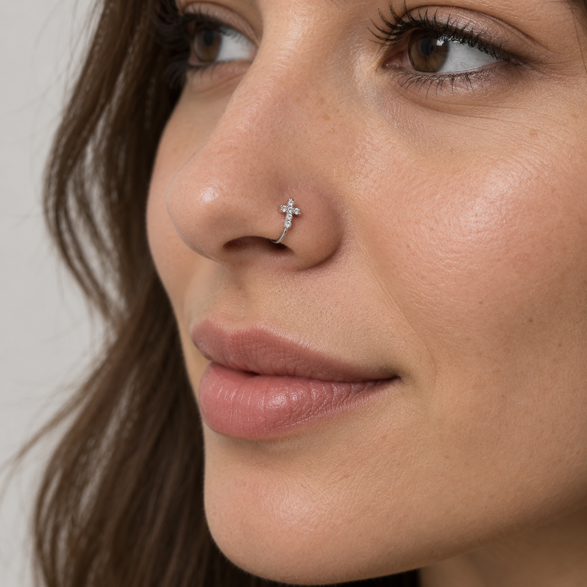 Woman wearing a petite upright silver crystal cross clip-on nose ring